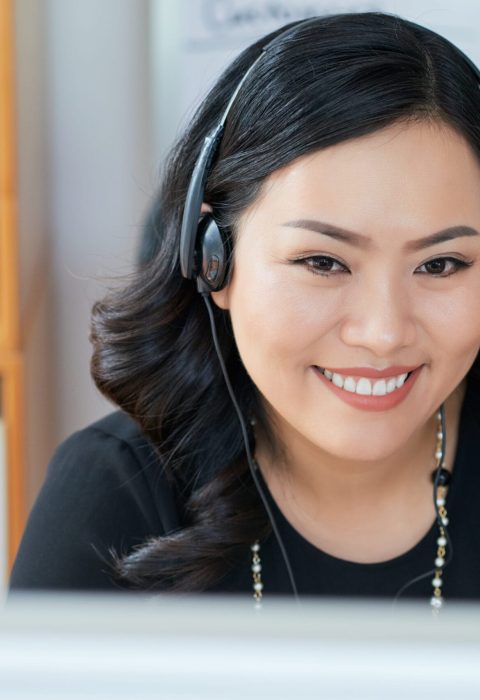 Attractive Asian businesswoman in headset reading data on computer screen