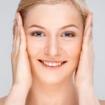 Close up portrait of young pretty girl over white background. Close up portrait of blonde young pretty girl, smiling, looking at camera, hands on cheeks, over white background.
