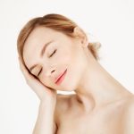 Portrait of young beautiful girl smiling with closed eyes touching face over white background. Facial treatment. Beauty cosmetology and spa. Portrait of young beautiful girl smiling with closed eyes touching face over white background. Facial treatment. Beauty cosmetology and spa. Copy space.